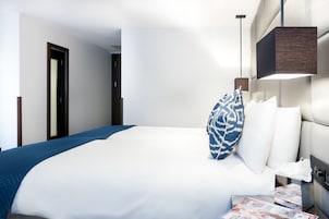 Ein Hotelzimmer mit einem großen Bett, einem Nachttisch mit Lampe und einer Tür zu einem weiteren Raum.