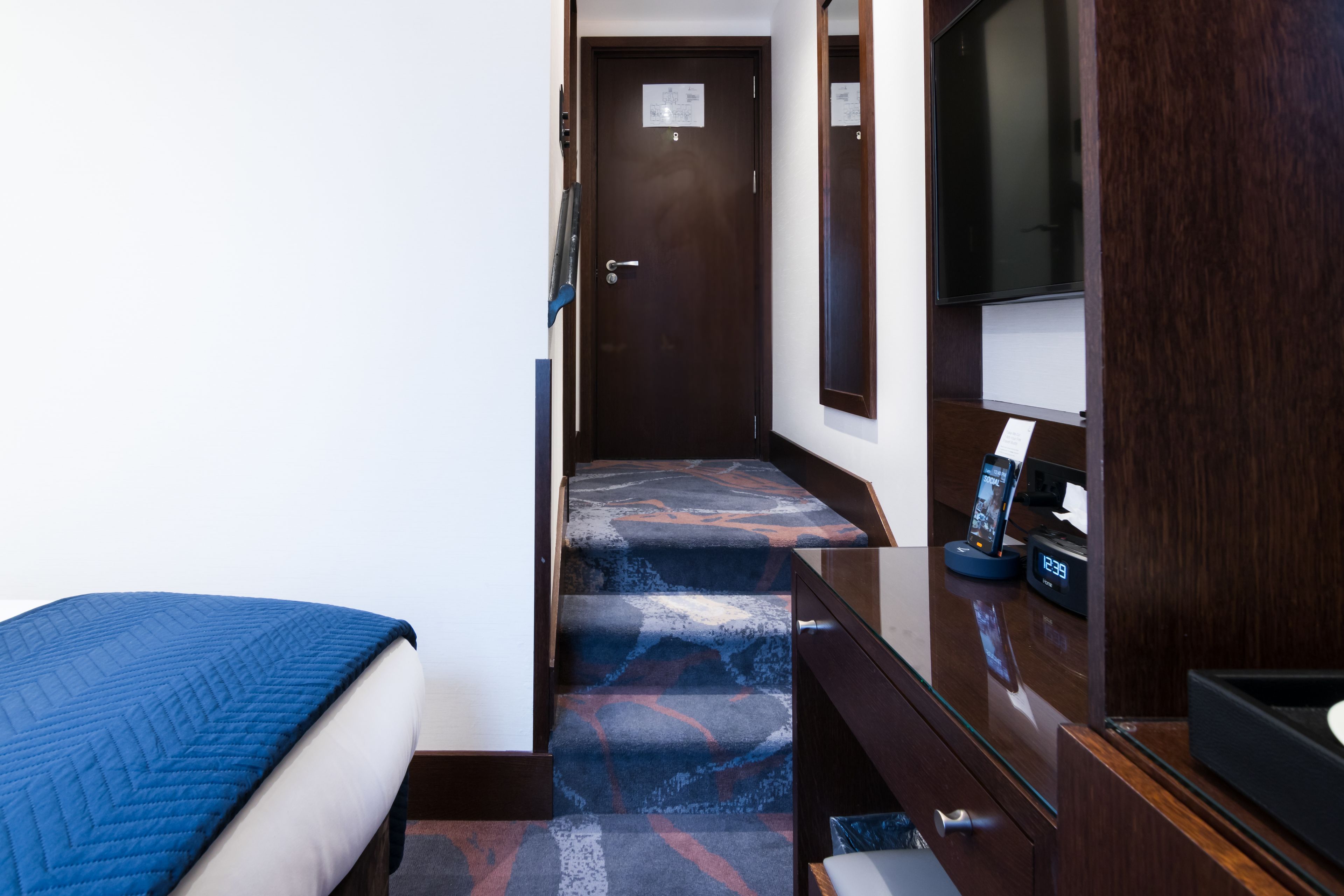 A hotel room with a bed, a desk with a computer and phone, a TV, and a staircase.