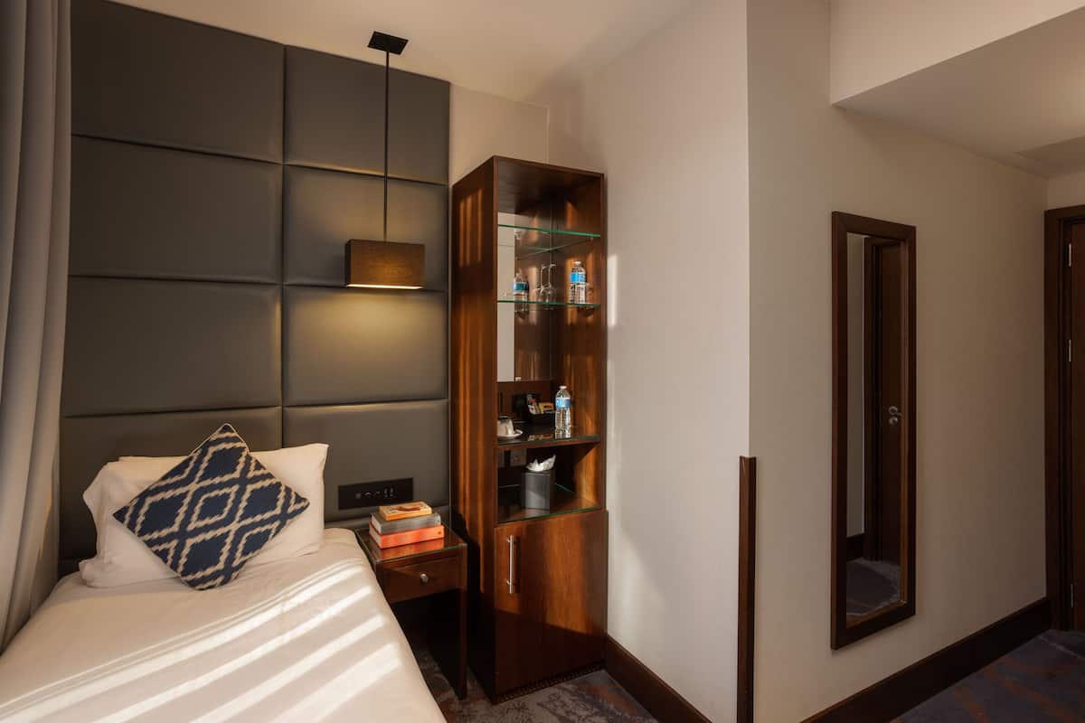 Habitación de hotel con cama, aparador de madera con estantes de vidrio, espejo y puerta.