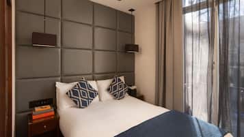 A modern hotel room with a large bed, a headboard with a padded back, a bedside table with a book, and a window with sheer curtains.