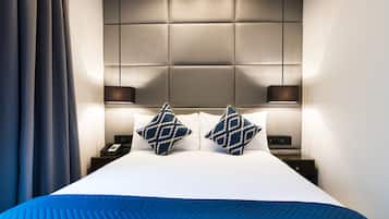 Habitación de hotel con una cama grande, cabecera acolchada, dos mesitas de noche con lámparas y una cortina a la izquierda.