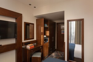 Habitación de hotel compacta con televisión de pantalla plana, armario de madera, microondas y cama con manta azul.