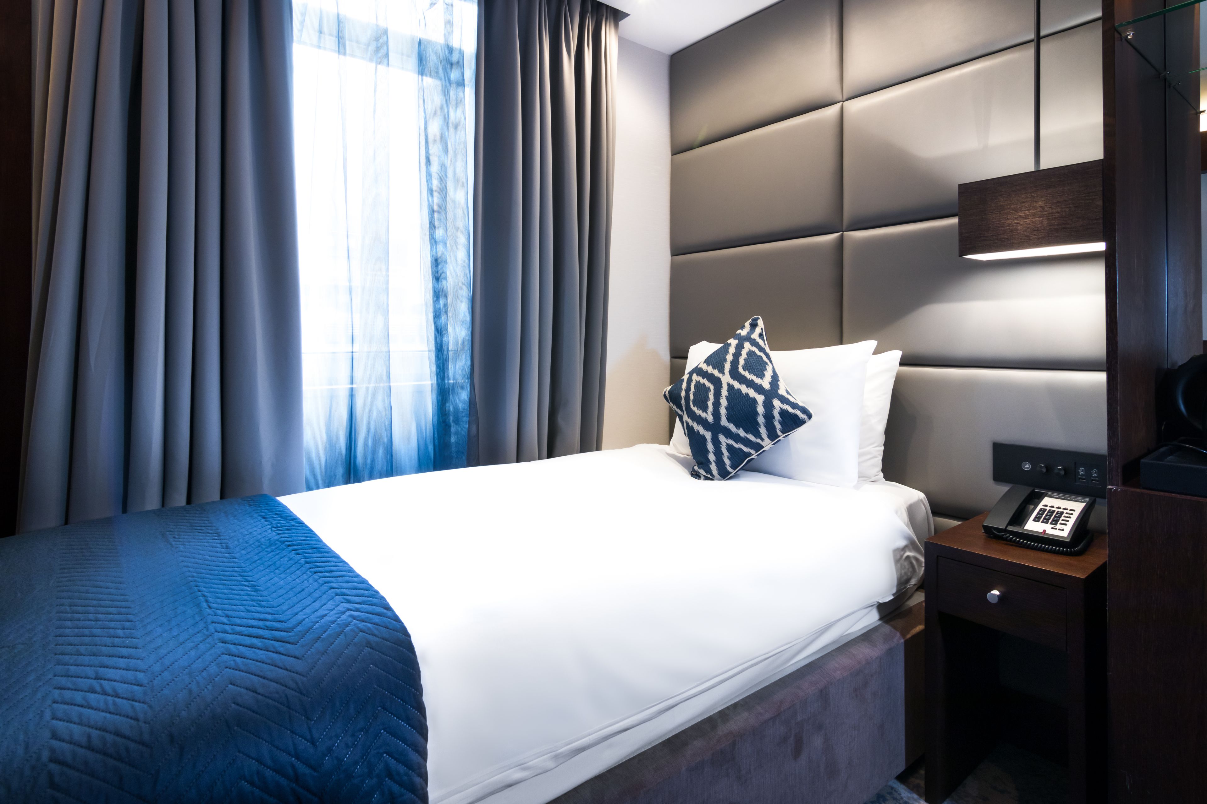 A hotel room with a bed, a bedside table with a phone, and a headboard.