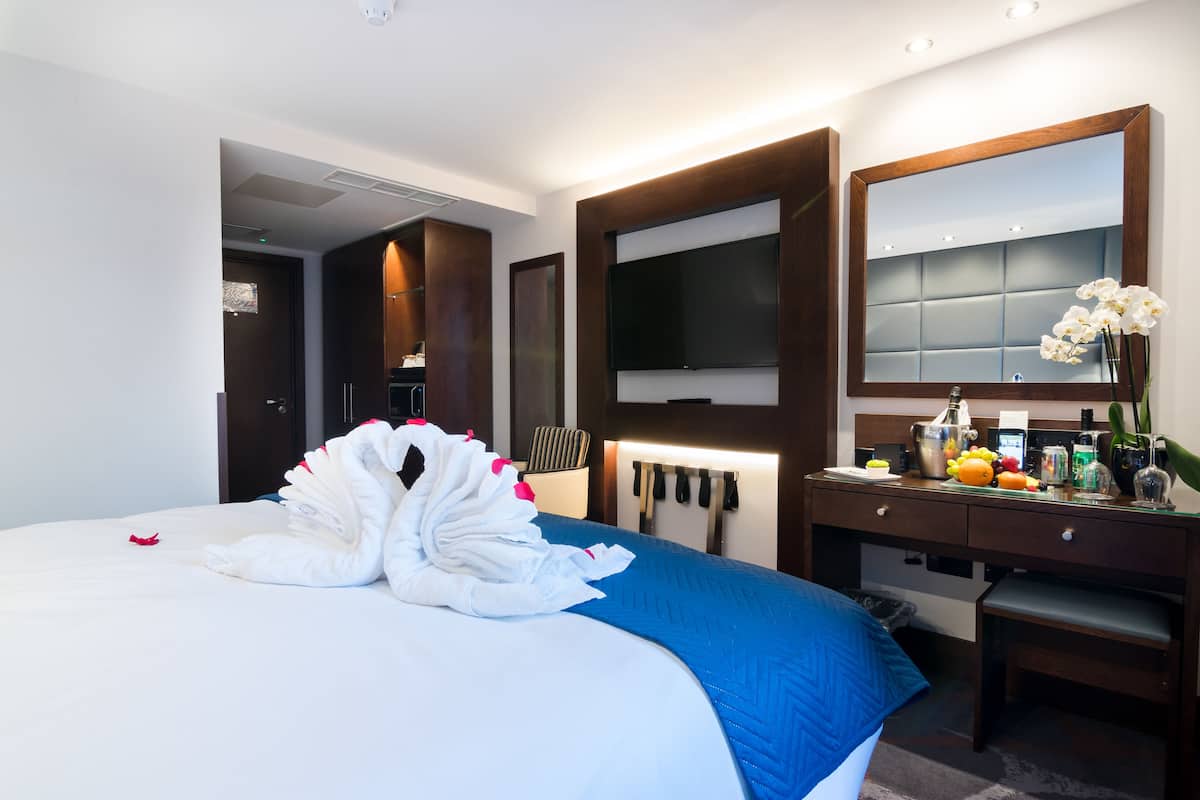 Habitación de hotel con una cama grande, un escritorio con espejo, un televisor de pantalla plana y un pequeño rincón de descanso.
