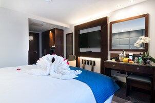 A hotel room with a large bed, a desk with a mirror, a flat-screen TV, and a small seating area.