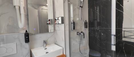 Ein modernes Badezimmer mit einem weißen Waschbecken, einer Handbrause und einer Duschkabine aus Glas.
