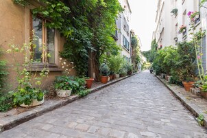 Una calle adoquinada flanqueada por edificios, macetas y cestas de flores colgantes.