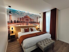 Habitación de hotel con una cama grande, un banco, un mural en la pared del Taj Mahal y vistas del cielo a través de cortinas translúcidas.