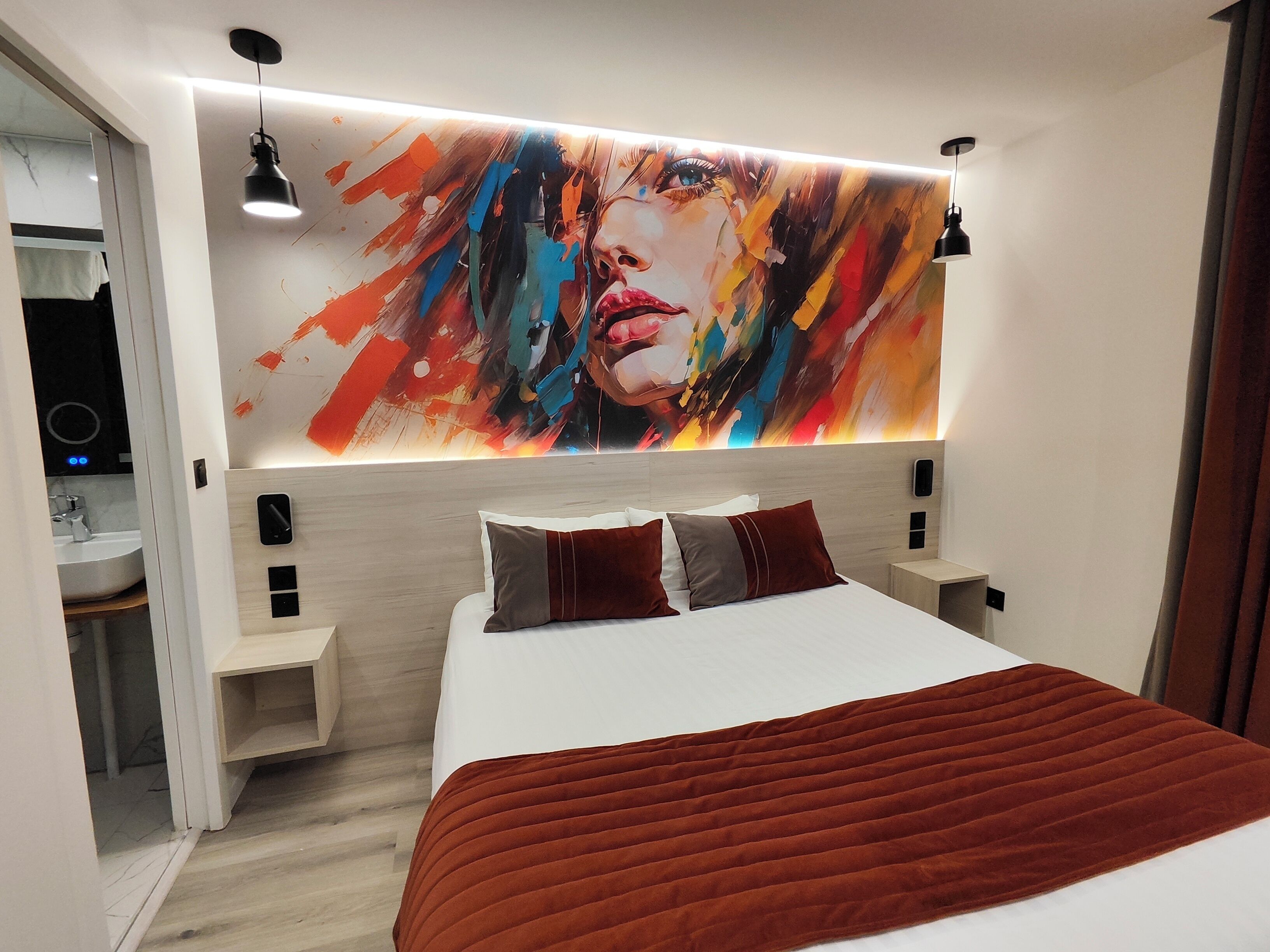 A modern bedroom with a large bed, a bedside table, a nightstand, and a wall-mounted artwork.