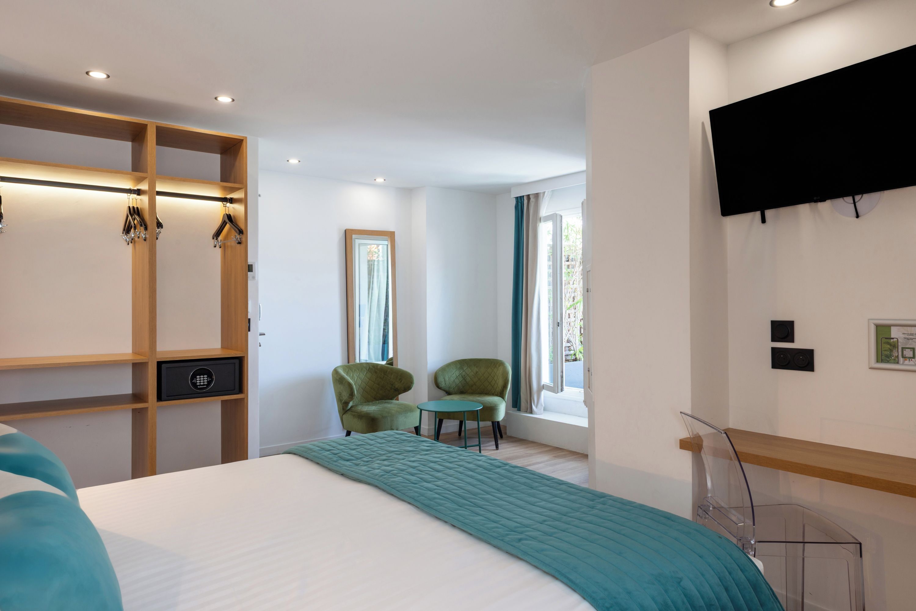 A hotel room with a bed, a seating area with chairs, a TV mounted on the wall, and a window with curtains.