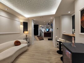 Una sala de estar moderna con un sofá, una mesa de centro y un televisor. Se ve una escalera que conduce a una zona de cocina con una encimera y un televisor.