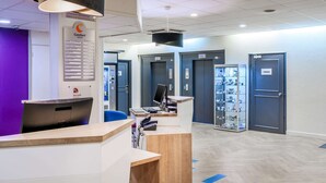 Ein Hotel-Rezeptionsbereich mit Empfangsschalter, Computer und einem Hinweisschild. Es gibt Türen mit den Aufschriften "Jardins" und "Chambres non-lumineuses".