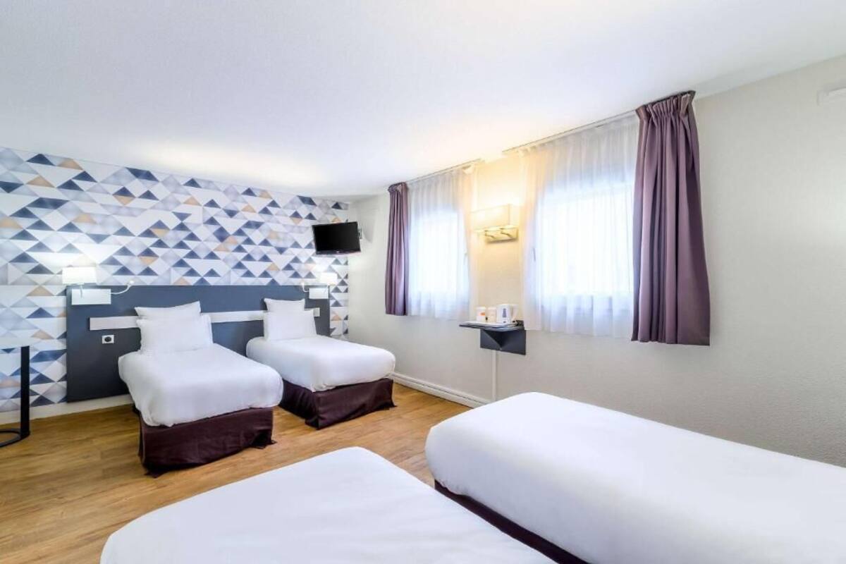 A hotel room with two beds, a geometric-patterned wall, a flat-screen TV, and a window with curtains.