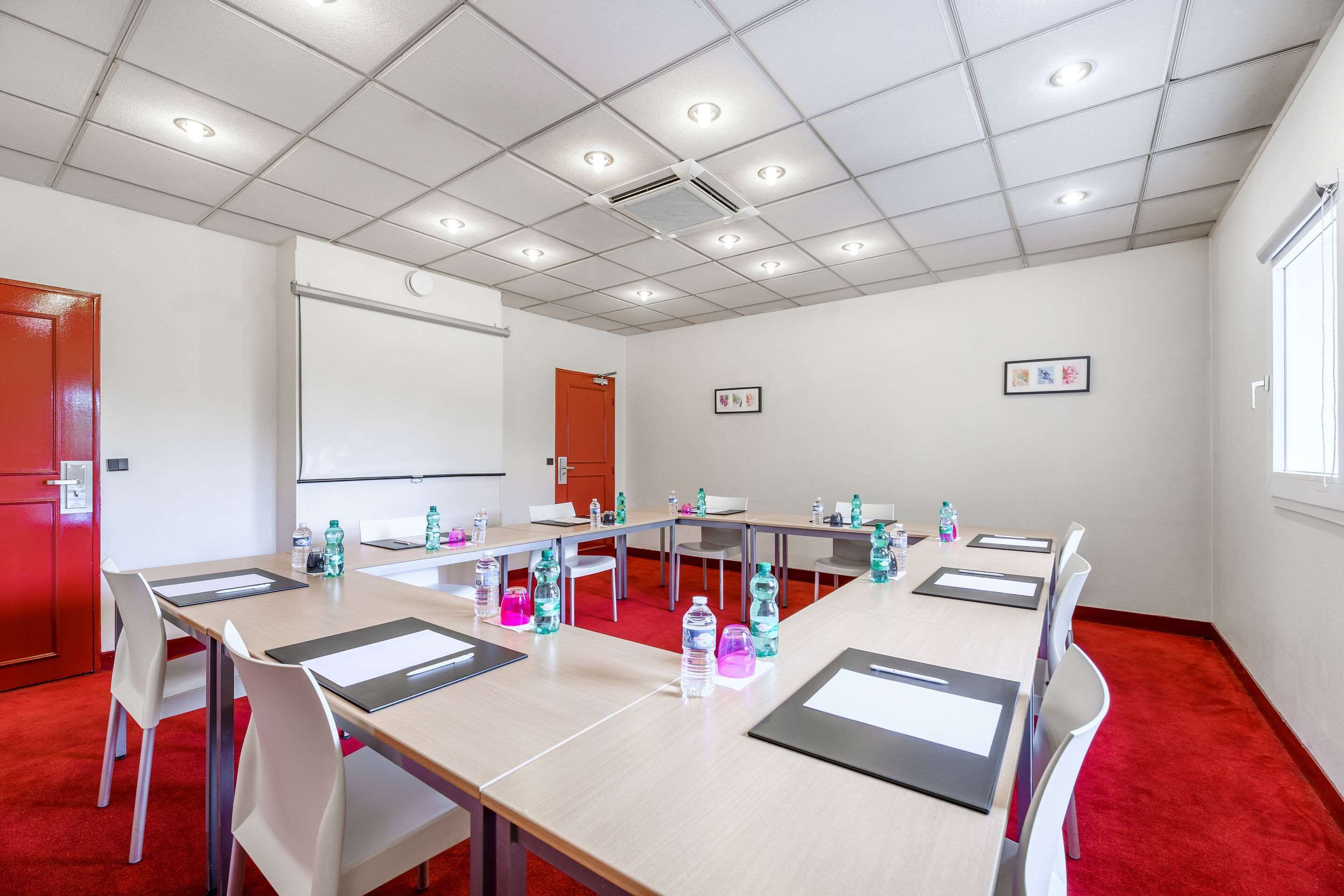 Ein Konferenzraum mit einem langen Tisch, Stühlen, einer Projektionsleinwand und einem roten Teppich.