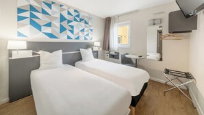 Ein Hotelzimmer mit zwei Betten, einem Fernseher, einem Schreibtisch und einem Fenster.