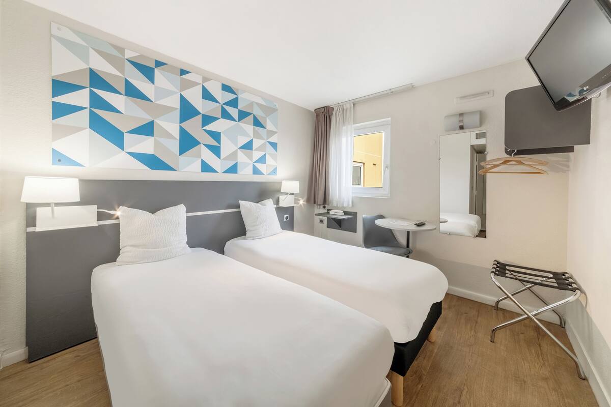 A hotel room with two beds, a TV, a desk, and a window.