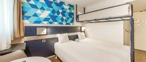 A hotel room with a bunk bed, a desk with a remote control, and a geometric-patterned wall.