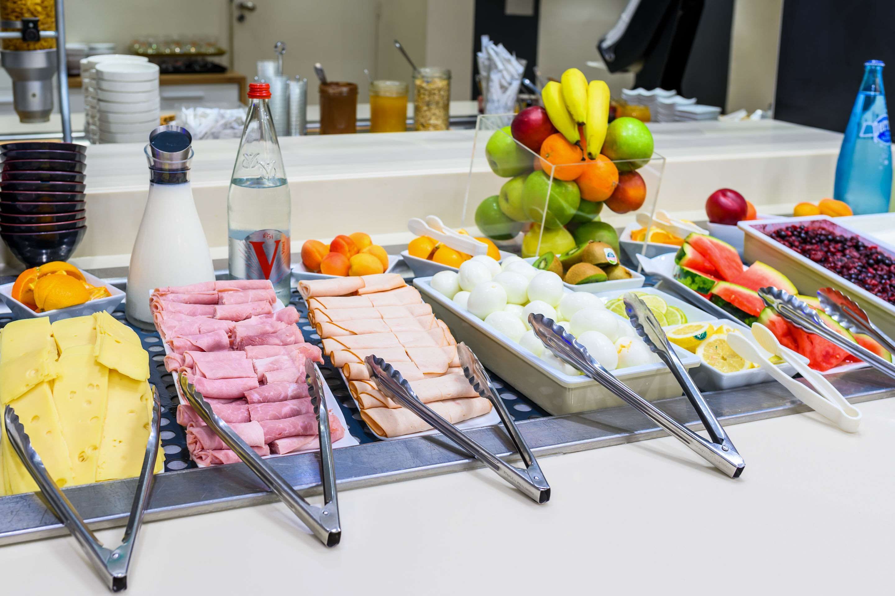 Un bufé con diversas opciones de comida, como carnes, quesos, frutas y verduras.