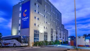 Ein Comfort Hotel mit einem großen Bus vor der Tür, einem gut beleuchteten Eingang und blauem Himmel.