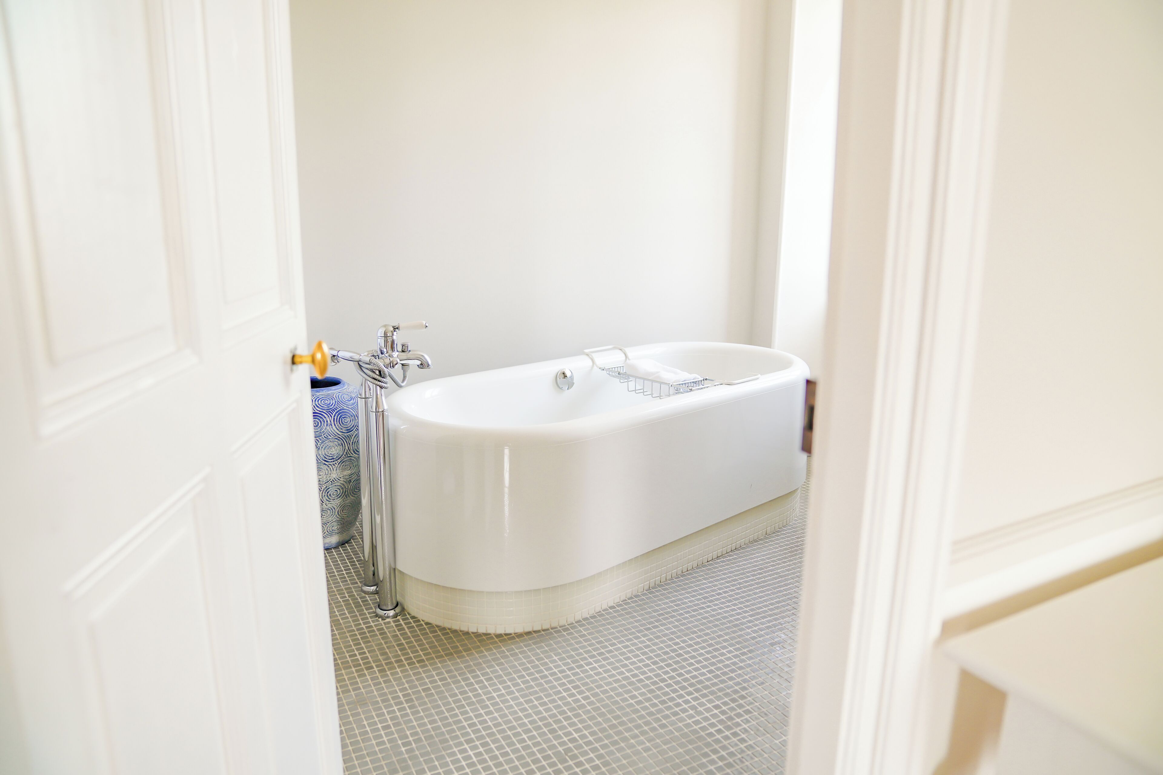 A bathroom with a white bathtub, a blue vase, and a tiled floor.