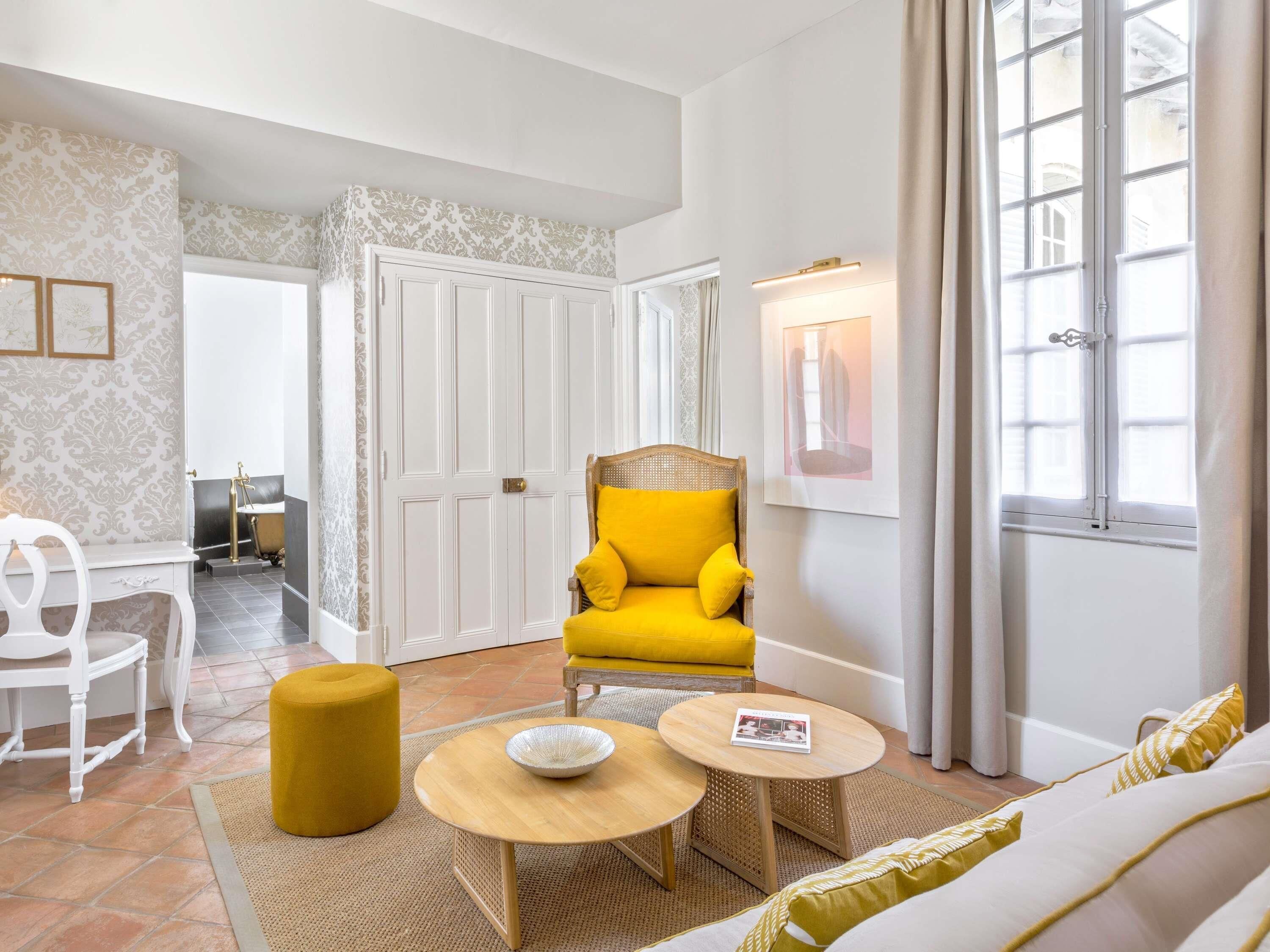 A modern living room with a yellow armchair, a white sofa, a wooden coffee table, and a small round table with a bowl.