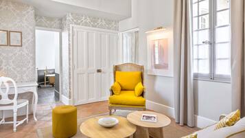 A modern living room with a yellow armchair, a white sofa, a wooden coffee table, and a small round table with a bowl.
