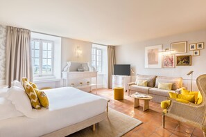 Una habitación de hotel con una cama grande, un sofá, un televisor y obras de arte en la pared.