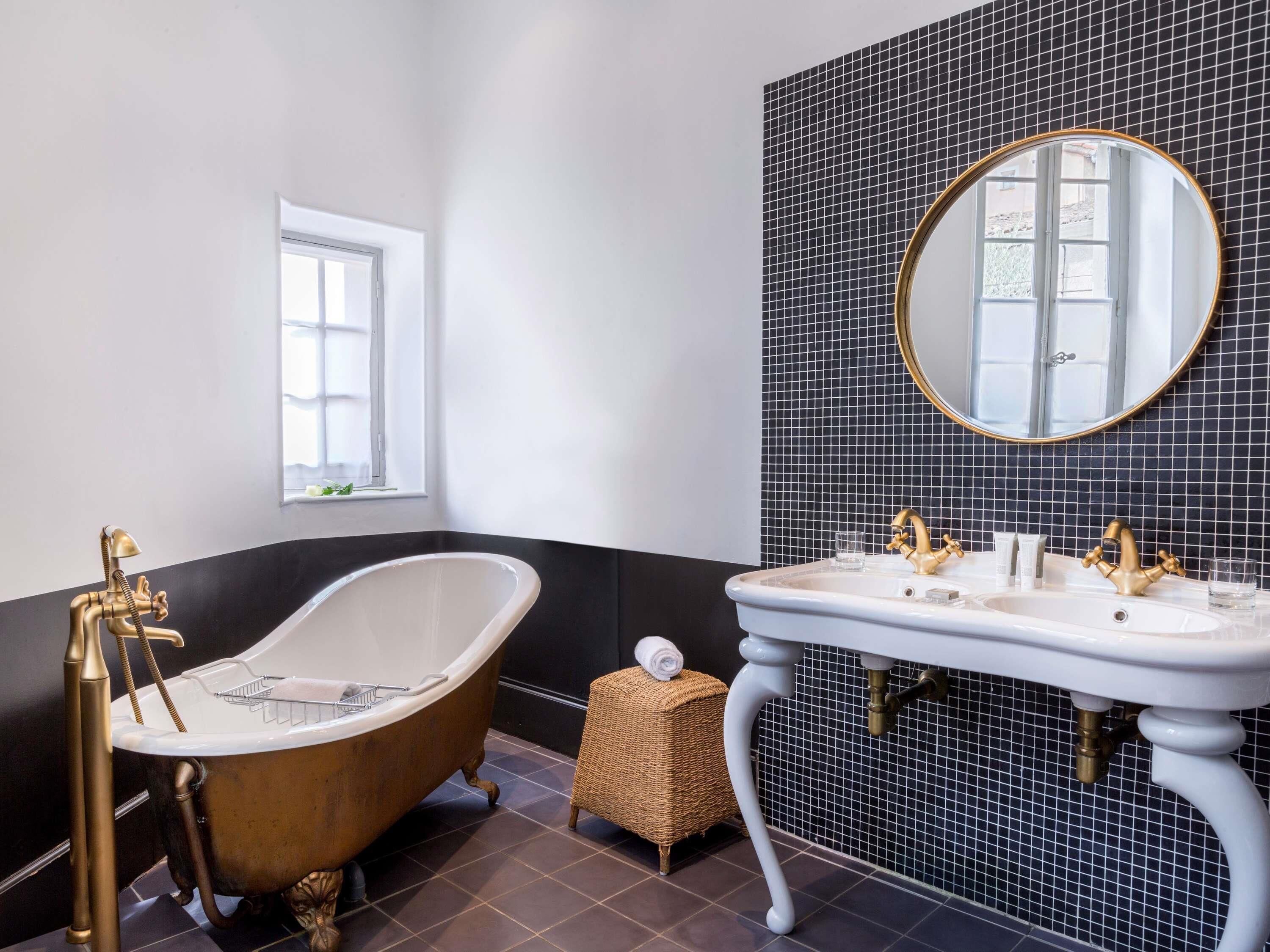 Une salle de bain avec une baignoire sur pieds, un lavabo sur colonne, un miroir rond et une fenêtre.