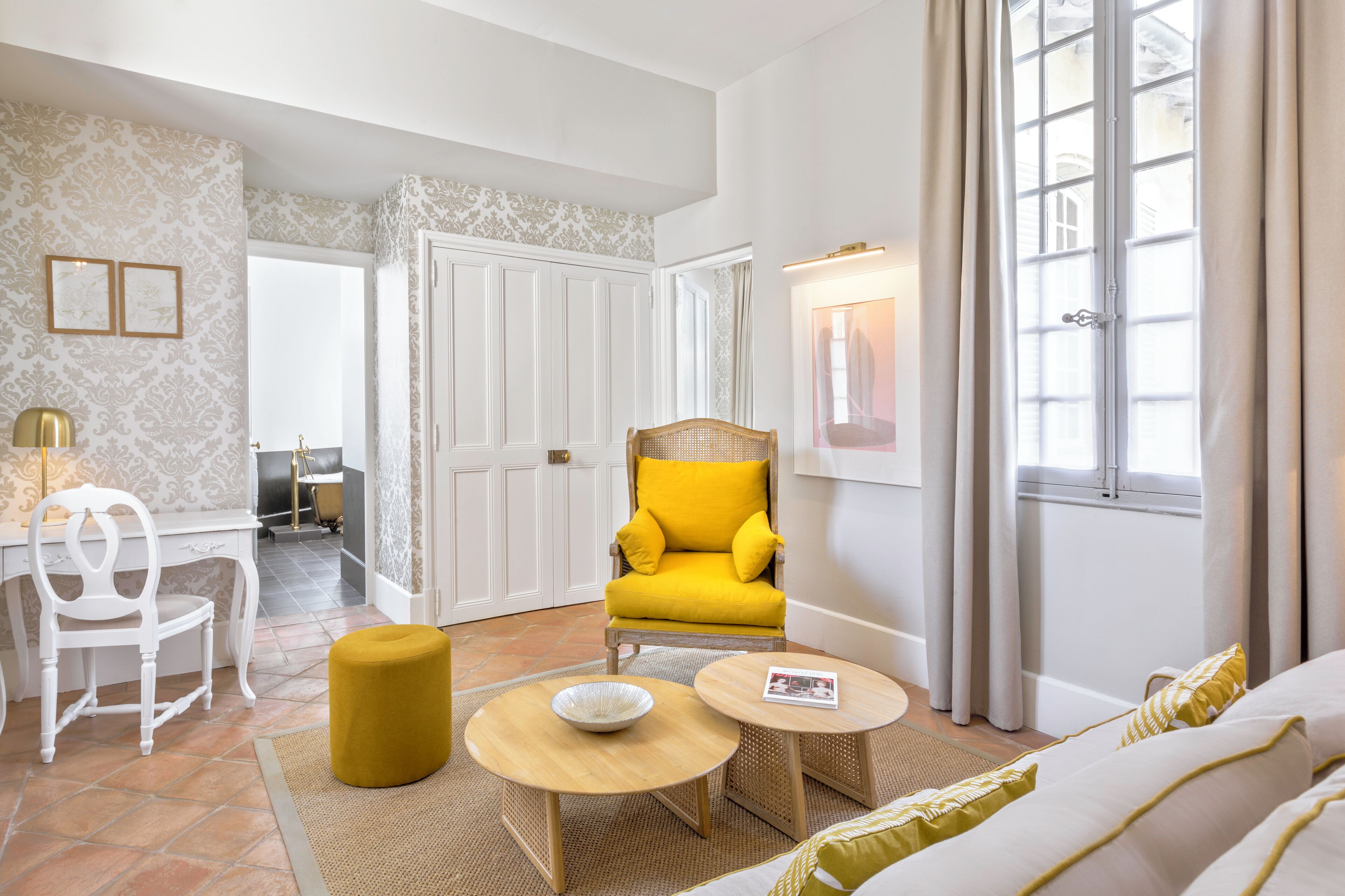 Una sala de estar moderna con un sillón amarillo, un sofá blanco y un comedor con mesa y sillas blancas.