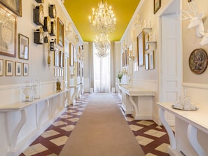 A hallway with a patterned floor, white walls, and a chandelier.