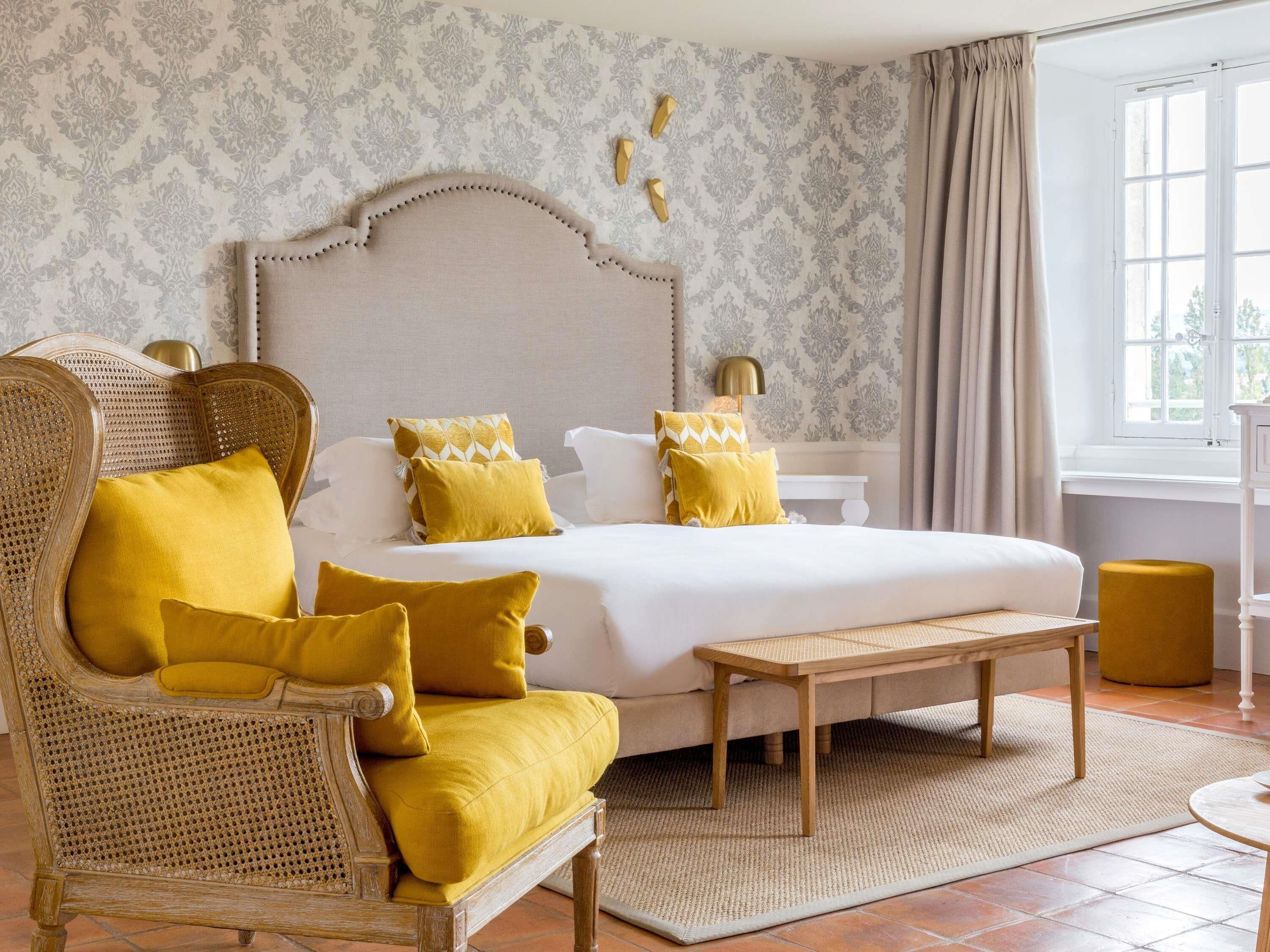 Een slaapkamer met een bed, een stoel, een nachtkastje, een lamp en een raam.