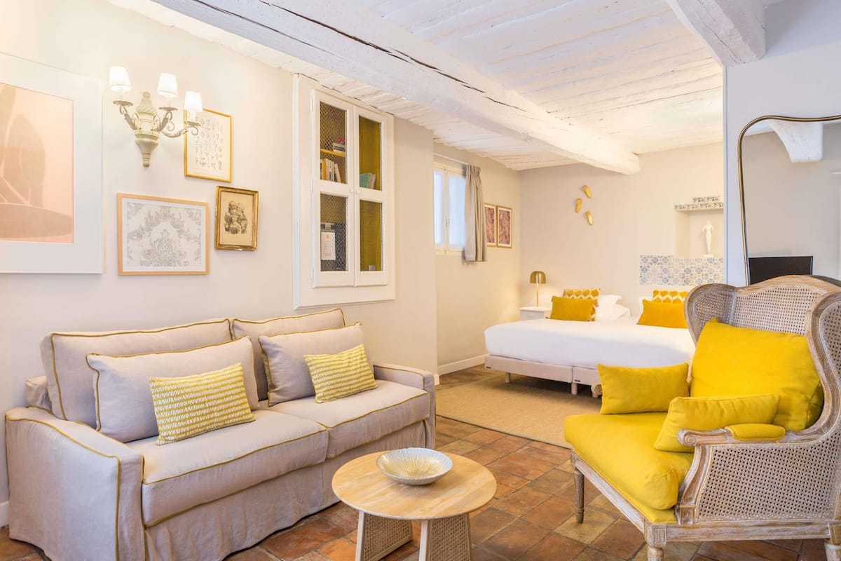 A room with a sofa, a chair, a bed, a small table, and a window.