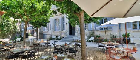An outdoor café with tables and chairs, surrounded by trees and buildings.