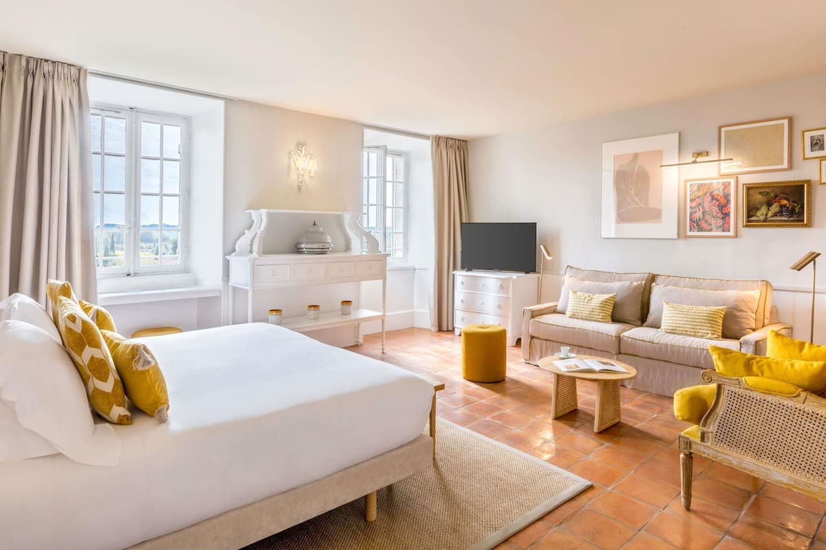 A hotel room with a bed, a sofa, a TV, a desk, and a window.