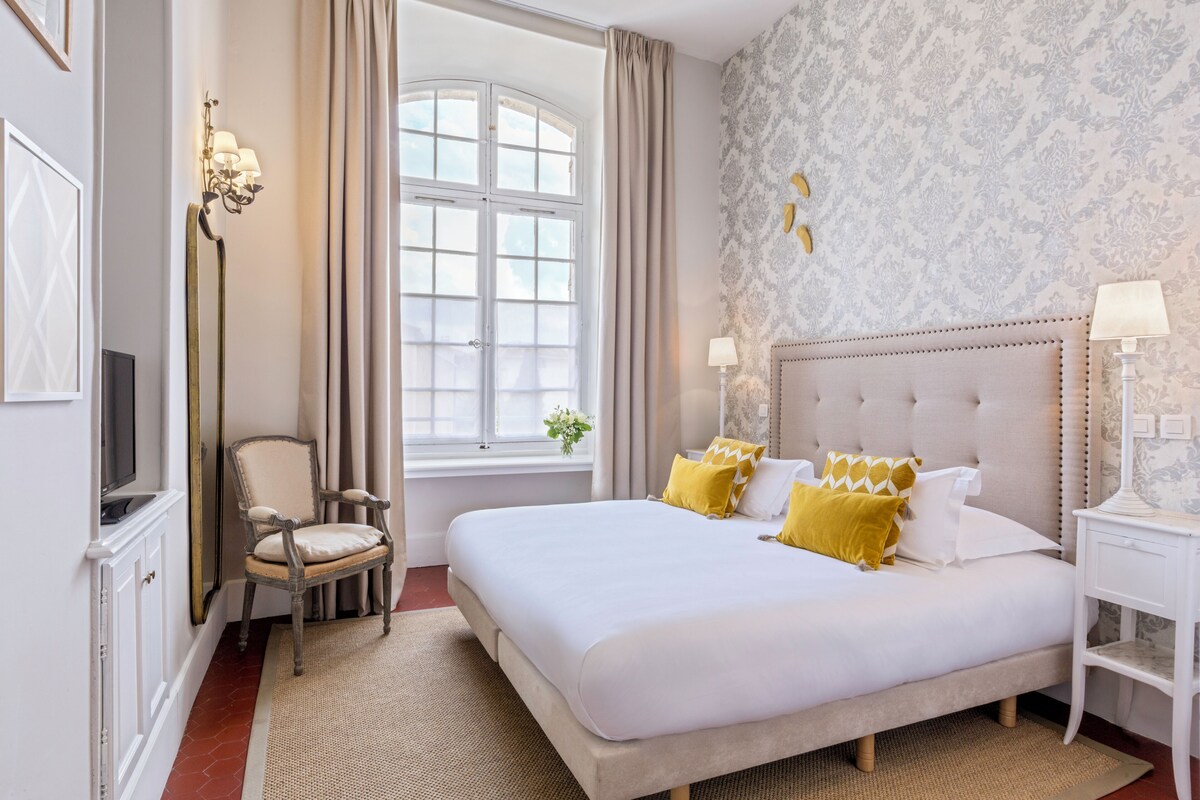 A hotel room with a large bed, a television, a chair, and a window with curtains.