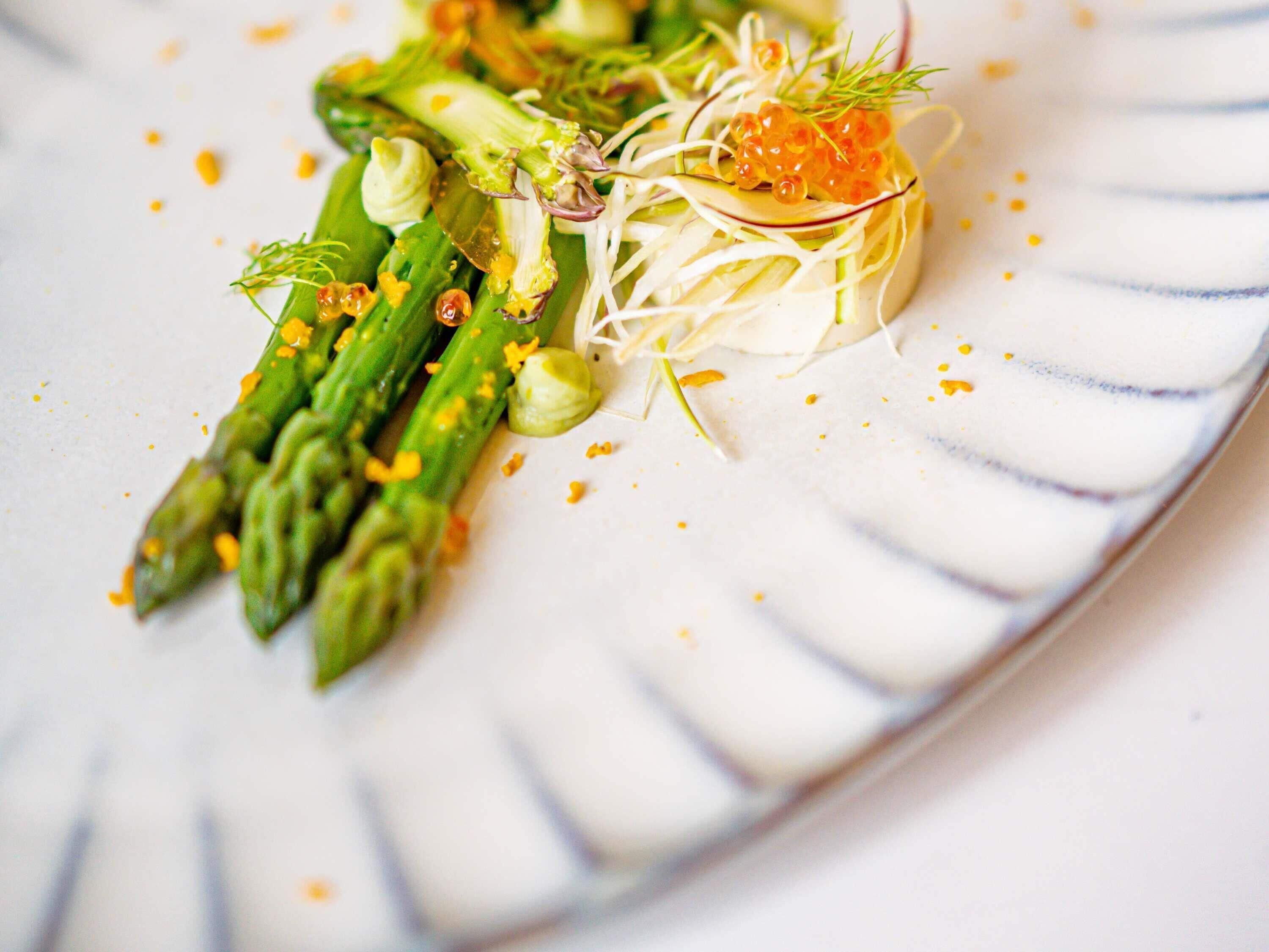 Een bord met een schotel asperges, spruiten en kaviaar.