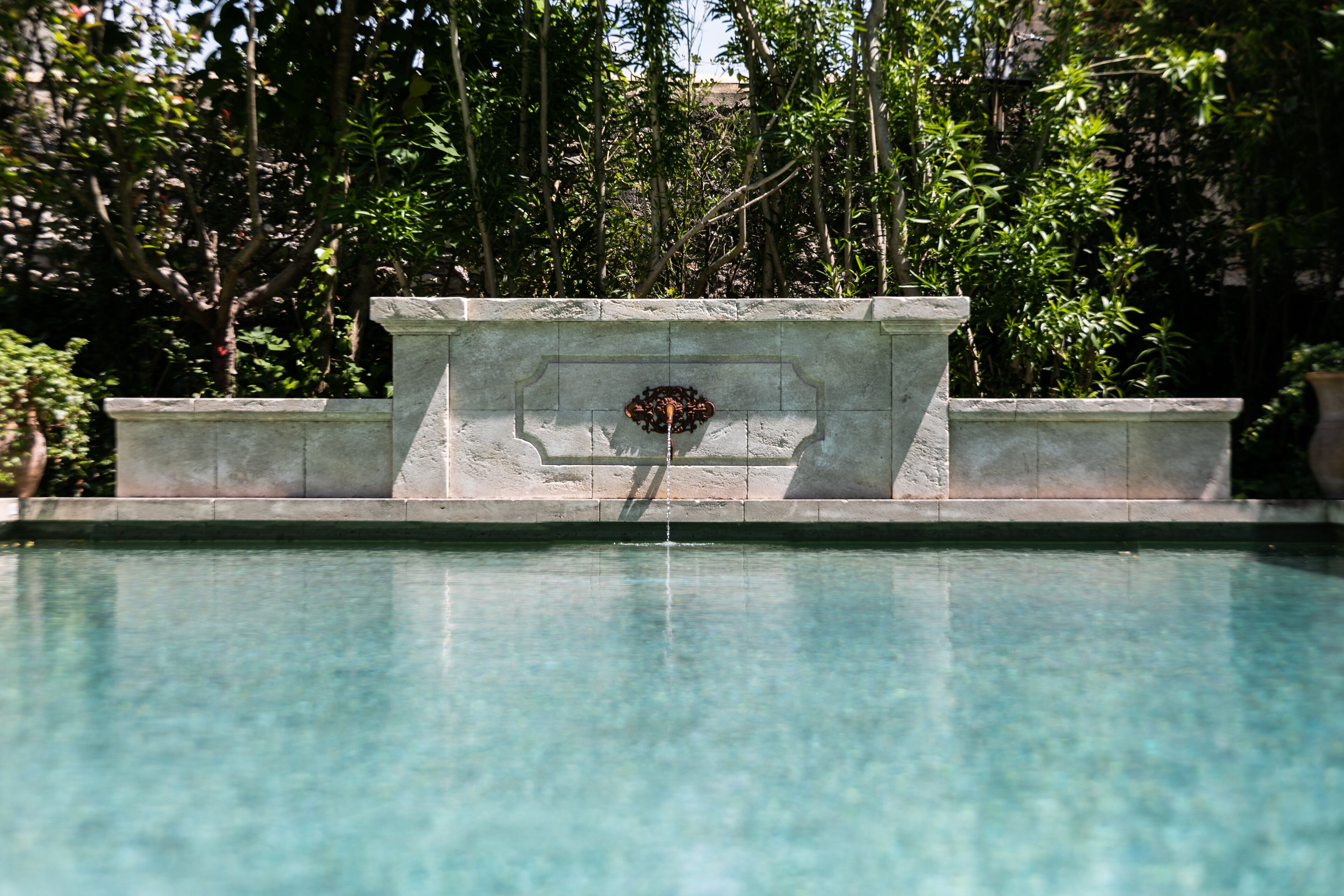 Une piscine aux eaux cristallines, avec une structure en pierre au centre, entourée d’une végétation luxuriante.