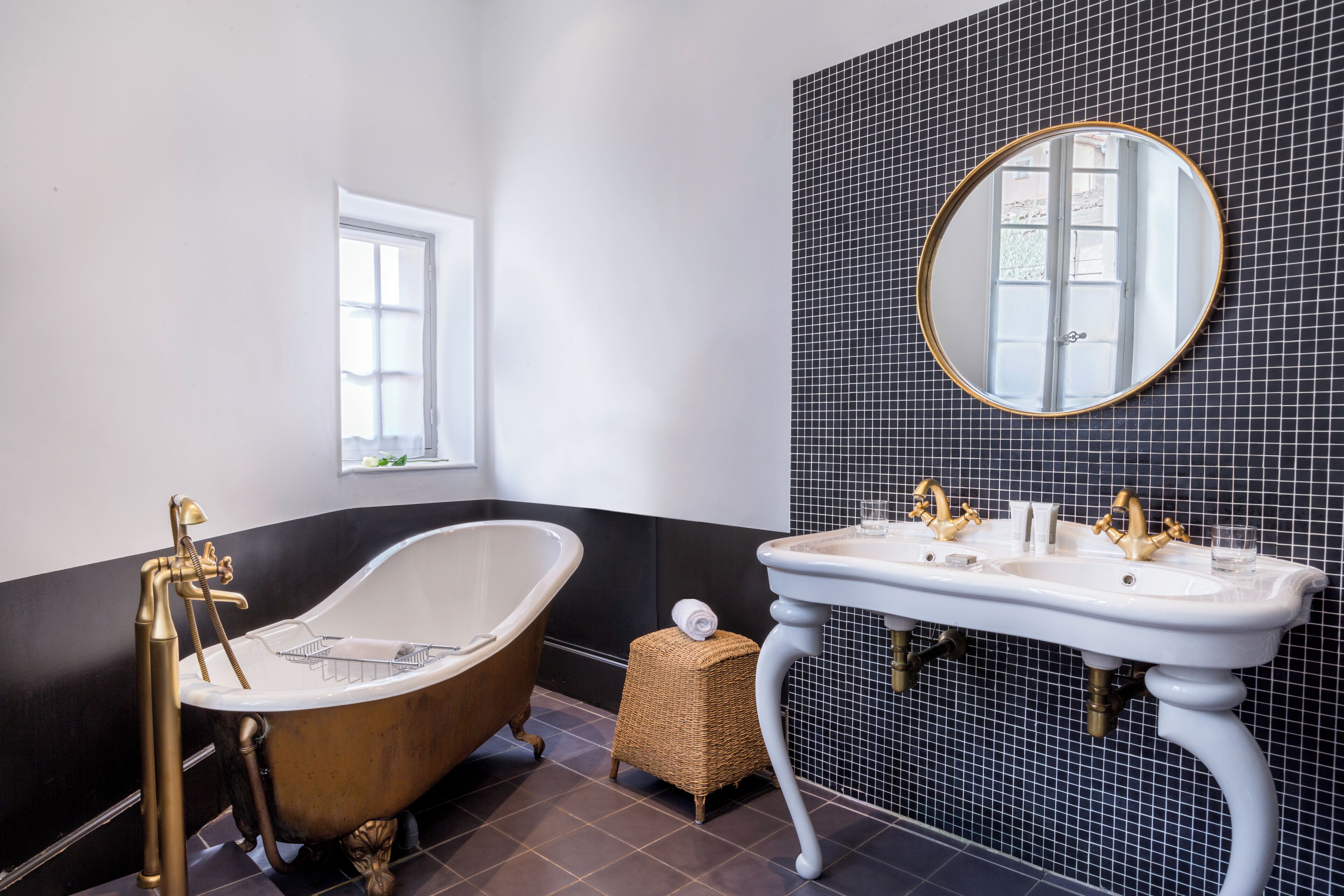 A bathroom with a freestanding bathtub, a white sink with gold fixtures, and a large mirror on the wall.