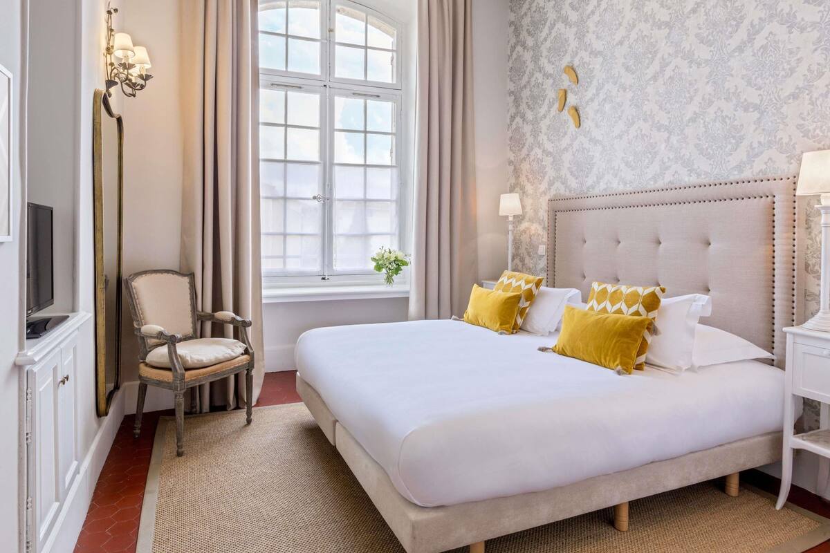 A hotel room with a large bed, a chair, a television, and a window with curtains.