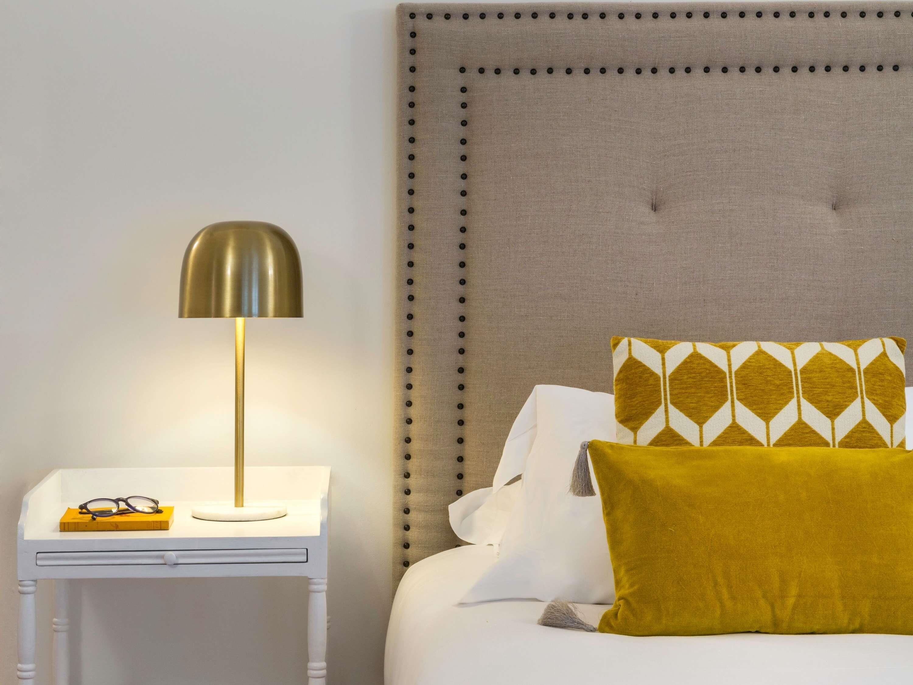 A neatly made bed with a tufted headboard, a bedside table with a lamp, and a patterned pillow.