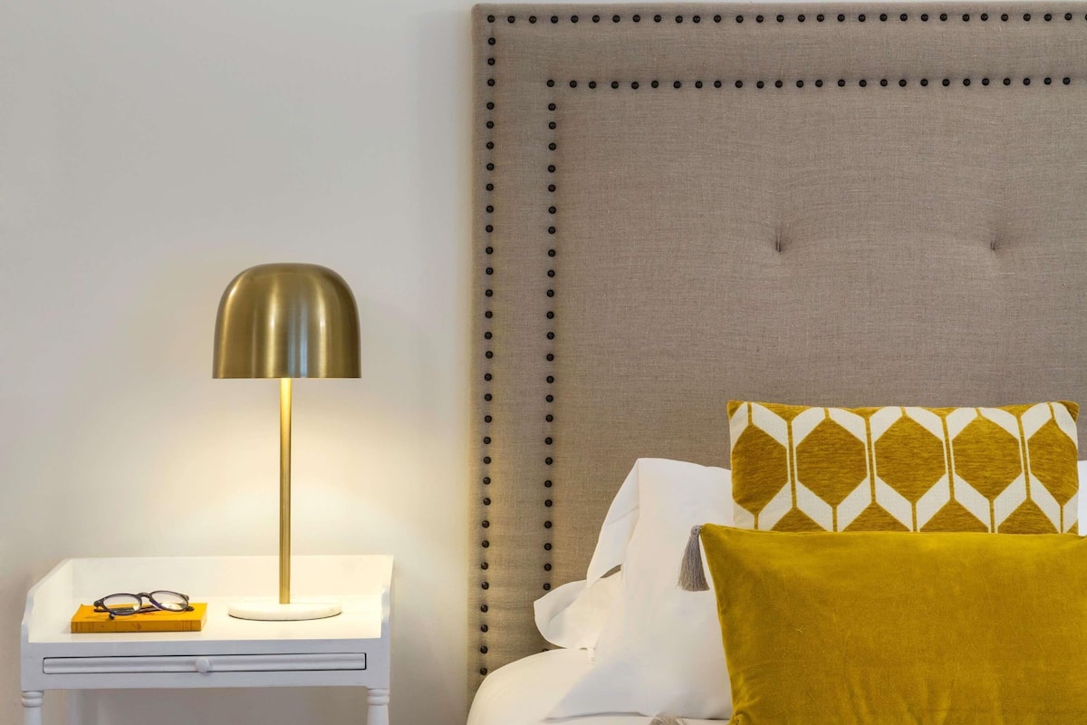 A neatly made bed with a tufted headboard, a bedside table with a lamp, and a patterned pillow.