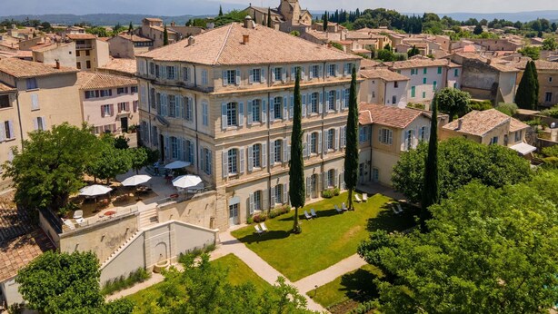 A large building with a prominent tower, surrounded by smaller buildings and greenery. - Chateau de Mazan - Handwritten Collection (Mazan)