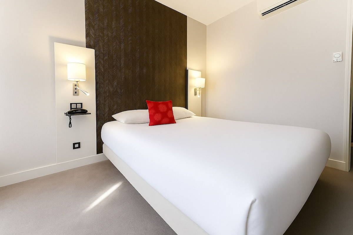 Habitación de hotel con una cama grande, dos lámparas de noche, una pared oscura con textura y un suelo de color claro.