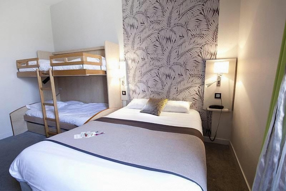 Une chambre d’hôtel avec des lits superposés, une table de chevet, une lampe et un papier peint à motifs.