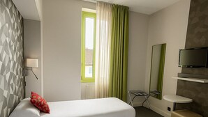 Une chambre d’hôtel avec deux lits, une télévision, une petite table et une fenêtre avec des rideaux.