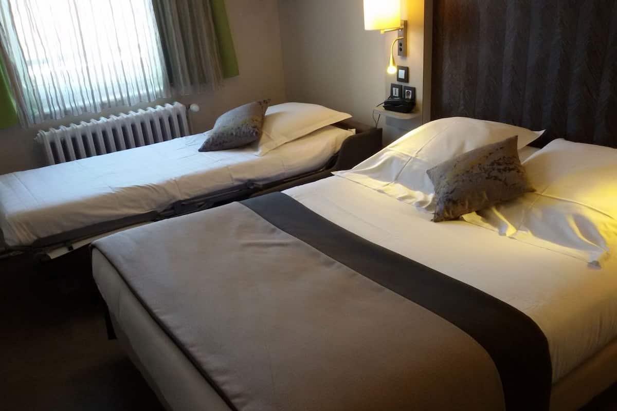 Habitación de hotel con dos camas, un radiador, una lámpara y una ventana con cortinas.