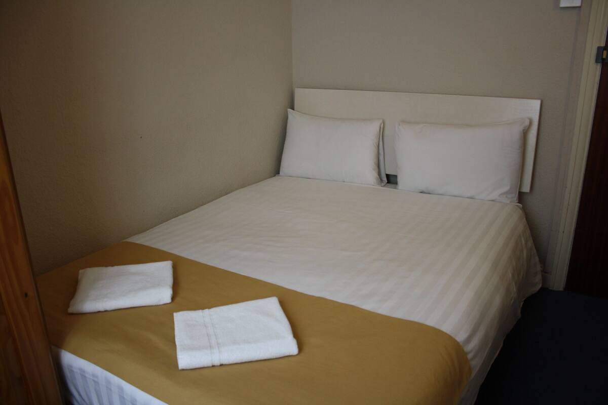 Una cama bien hecha con sábanas blancas y una colcha marrón, junto con dos toallas blancas dobladas.
