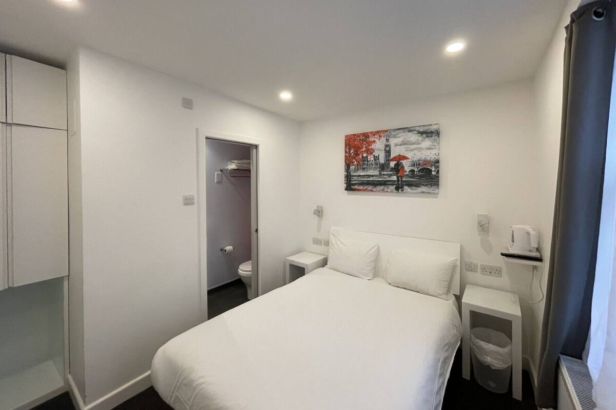 Habitación de hotel con cama, un cuadro en la pared, una mesita con una taza y un armario.