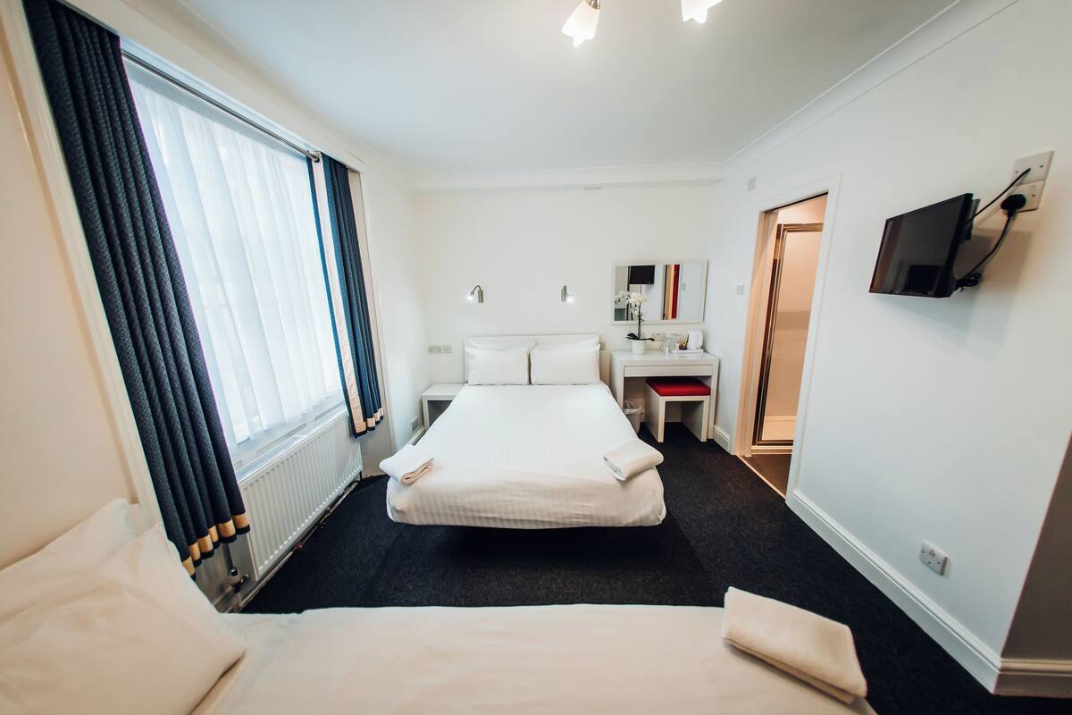 Habitación de hotel con cama, escritorio, silla, televisor y ventana con cortinas.