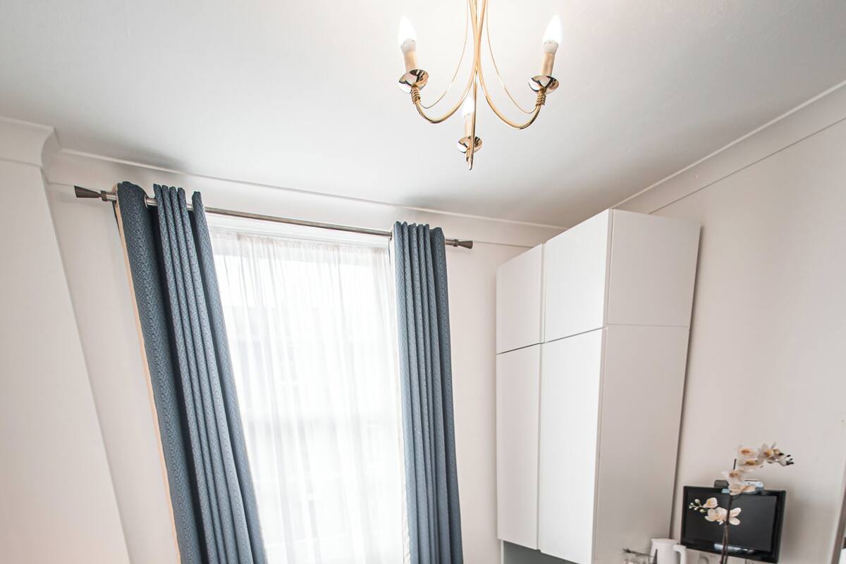 Habitación de hotel con una cama grande, un escritorio con ordenador, un espejo y una ventana con cortinas.